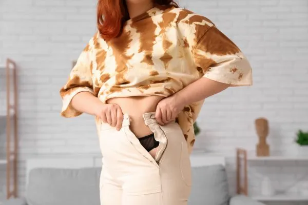 Image of woman trying to do her trousers up after pregnancy weight gain Iver